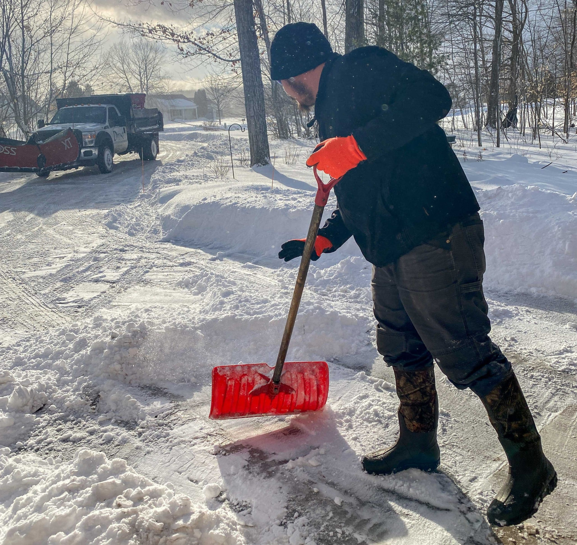 Hand clearing a snow-covered walkway with a red shovel